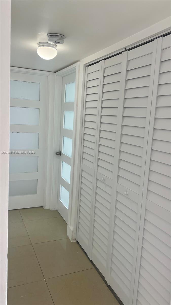 A hallway features light-colored tile flooring, two white doors with glass panels, and louvered closet doors — 488 NW 165th St Rd # 309, Miami FL 33169, MIAMI, FL