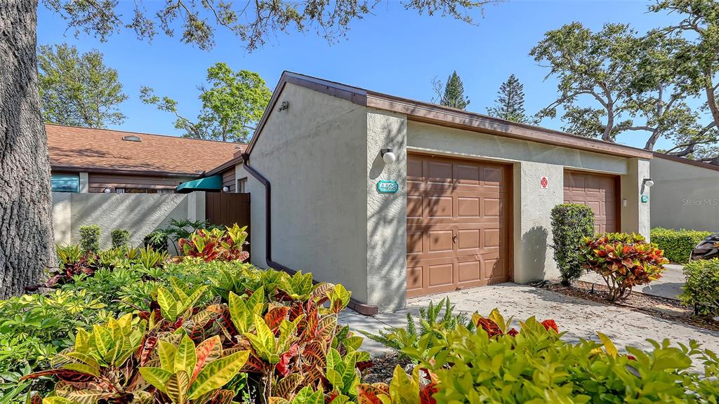 A tan stucco building features two brown garage doors and lush landscaping in the foreground — 4423 PARK LAKE TERRACE N, BRADENTON, FL
