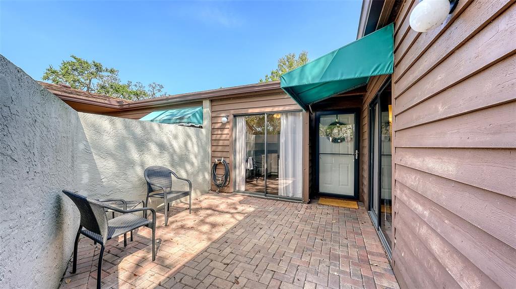 A brick patio features two chairs, a sliding glass door, and a green fabric awning — 4423 PARK LAKE TERRACE N, BRADENTON, FL