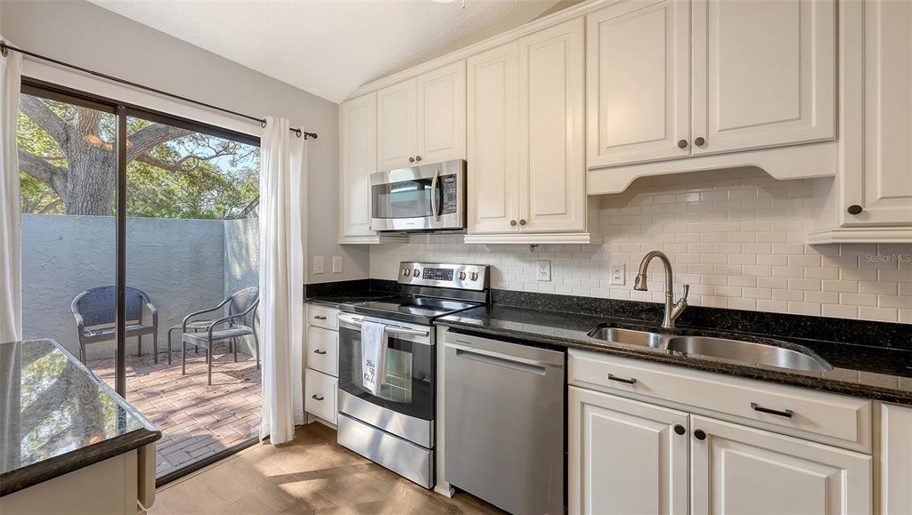 A kitchen with white cabinets, stainless steel appliances, black countertops, and a sliding glass door — 4423 PARK LAKE TERRACE N, BRADENTON, FL