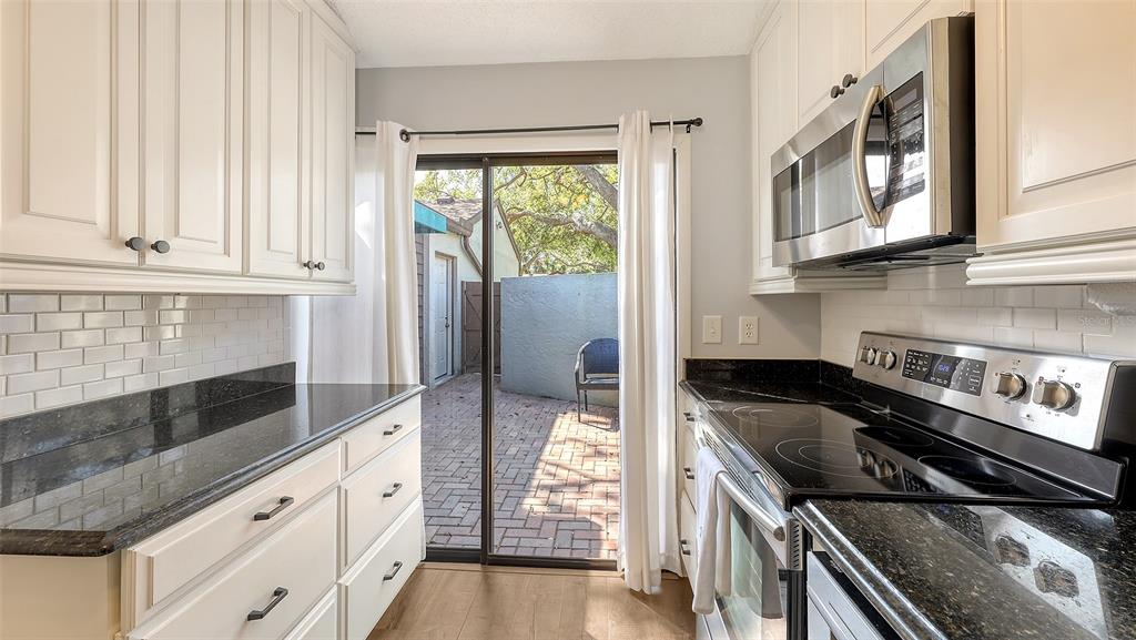A galley kitchen features white cabinets, black granite countertops, stainless steel appliances, and sliding glass doors — 4423 PARK LAKE TERRACE N, BRADENTON, FL