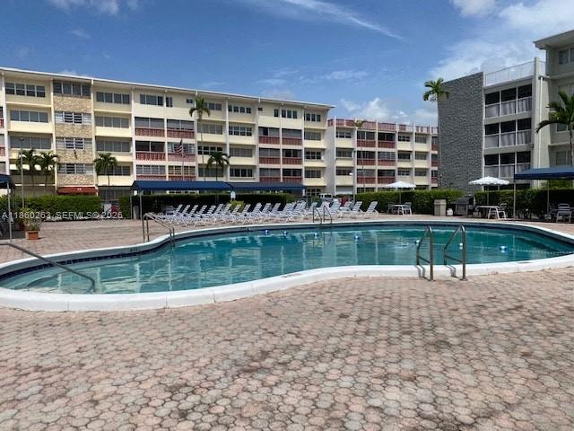 A swimming pool with lounge chairs sits in front of a multi-story apartment building — 215 SE 3rd Ave # 305A, Hallandale Beach FL 33009, HALLANDALE BEACH, FL