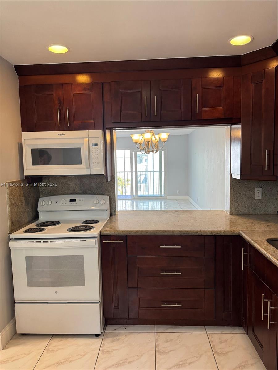 A kitchen features dark wood cabinets, granite countertops, and white appliances with a pass-through window — 215 SE 3rd Ave # 305A, Hallandale Beach FL 33009, HALLANDALE BEACH, FL