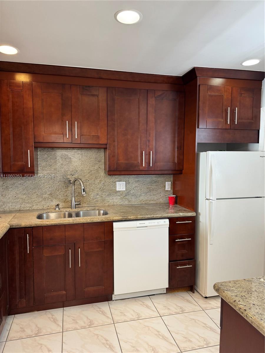 A kitchen features dark wood cabinets, granite countertops, a white dishwasher, and a white refrigerator — 215 SE 3rd Ave # 305A, Hallandale Beach FL 33009, HALLANDALE BEACH, FL
