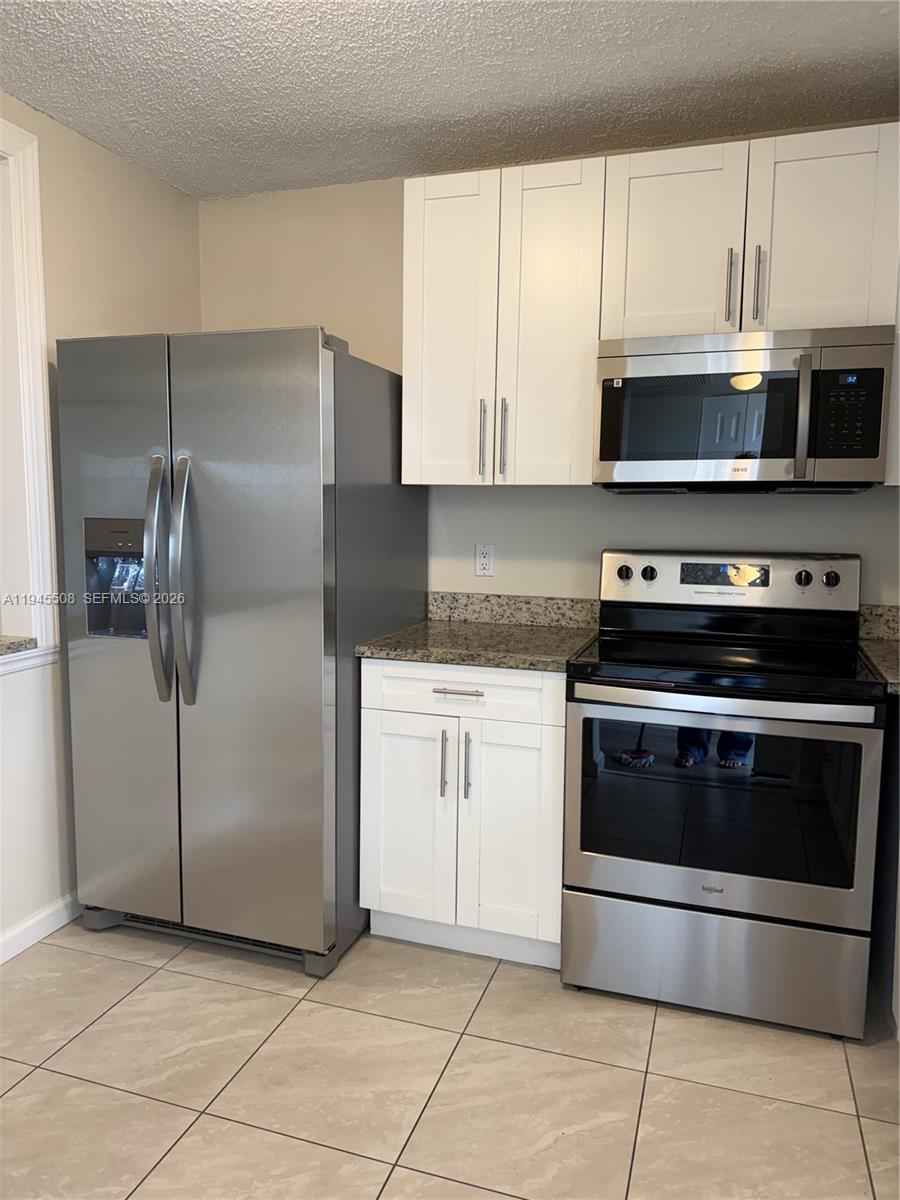 A kitchen features white cabinets, stainless steel appliances, and granite countertops over tiled floors — 9273 SW 8th St # 411, Boca Raton FL 33428, BOCA RATON, FL
