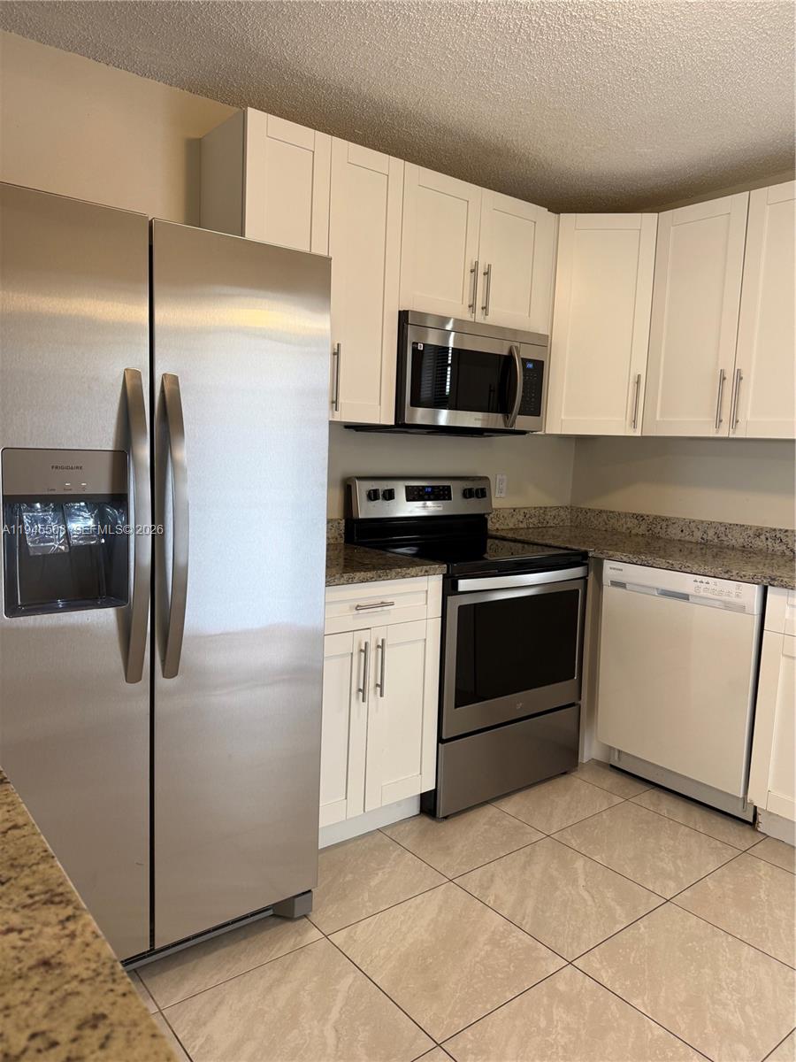 A kitchen features white cabinets, stainless steel appliances, and light-colored tile flooring — 9273 SW 8th St # 411, Boca Raton FL 33428, BOCA RATON, FL