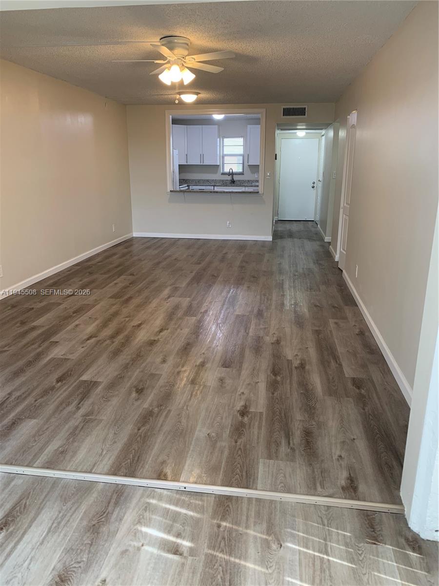An empty living room features wood-look laminate flooring and a pass-through window to the kitchen — 9273 SW 8th St # 411, Boca Raton FL 33428, BOCA RATON, FL