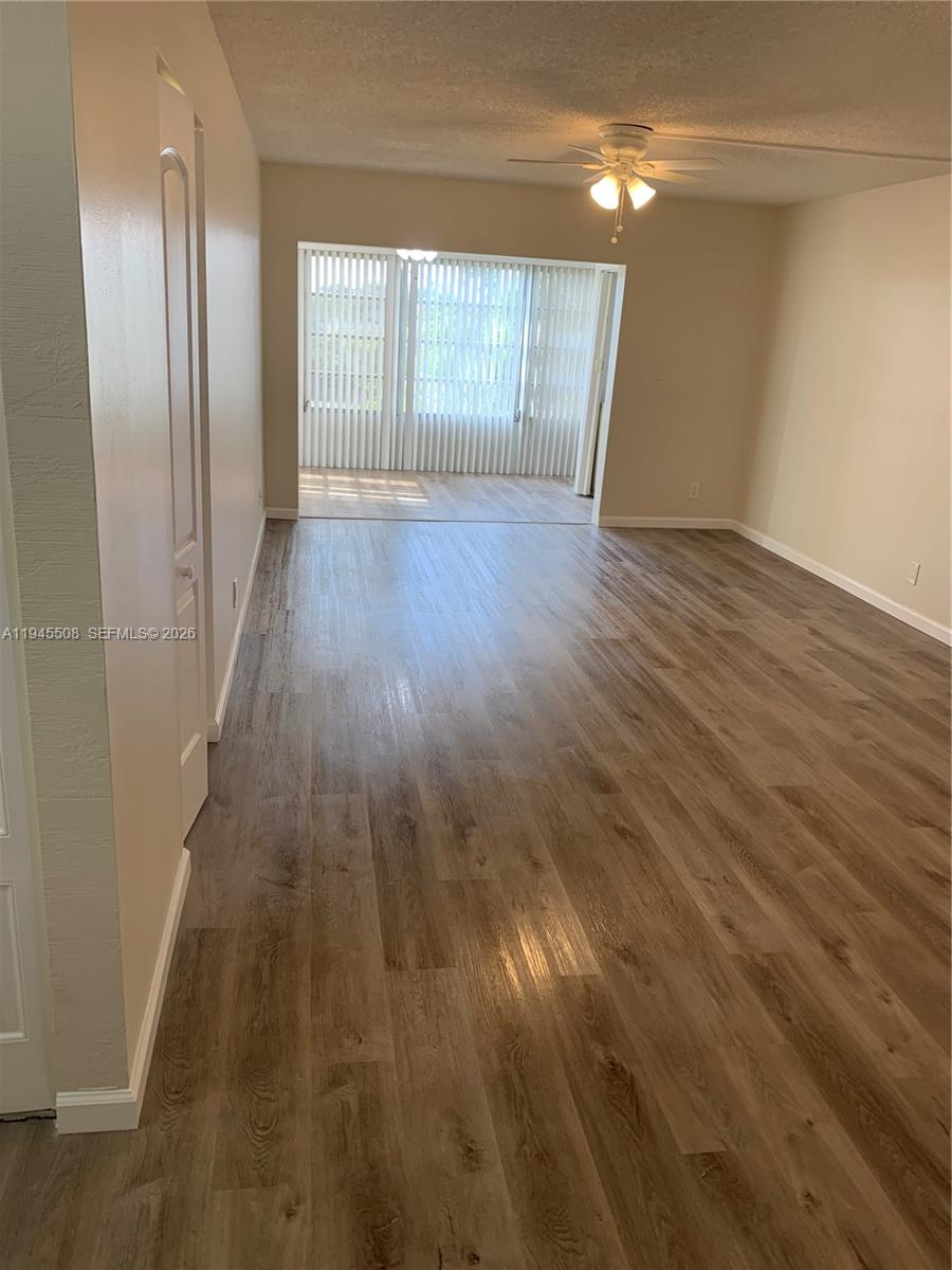 This living room features wood-look flooring, a ceiling fan, and a sliding glass door entrance — 9273 SW 8th St # 411, Boca Raton FL 33428, BOCA RATON, FL
