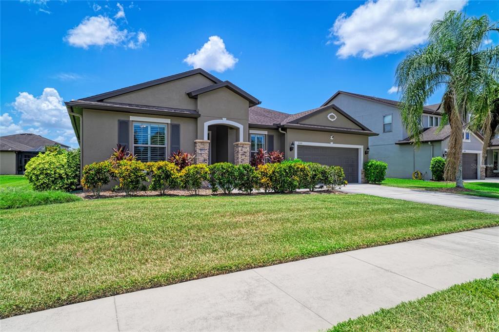 A single-story suburban house with a tan stucco exterior, a two-car garage, and landscaped bushes — 11101 58TH STREET CIRCLE E, PARRISH, FL