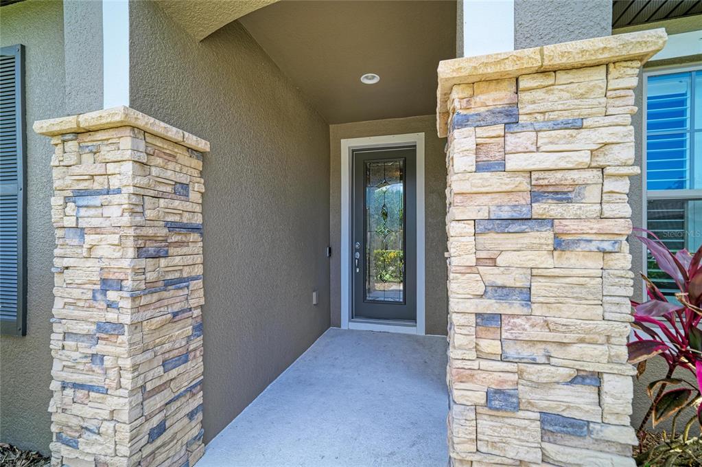 A covered entryway features a gray front door with a decorative glass insert between stone-clad pillars — 11101 58TH STREET CIRCLE E, PARRISH, FL