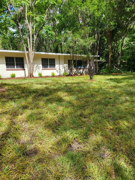 A single-story house with a white exterior and large windows sits behind a grassy lawn — 640 NW 36TH TERRACE, GAINESVILLE, FL