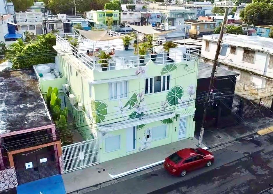 An aerial view of a light green three-story building featuring lime-themed murals and a rooftop terrace — 107 LOIZA, SAN JUAN, PR