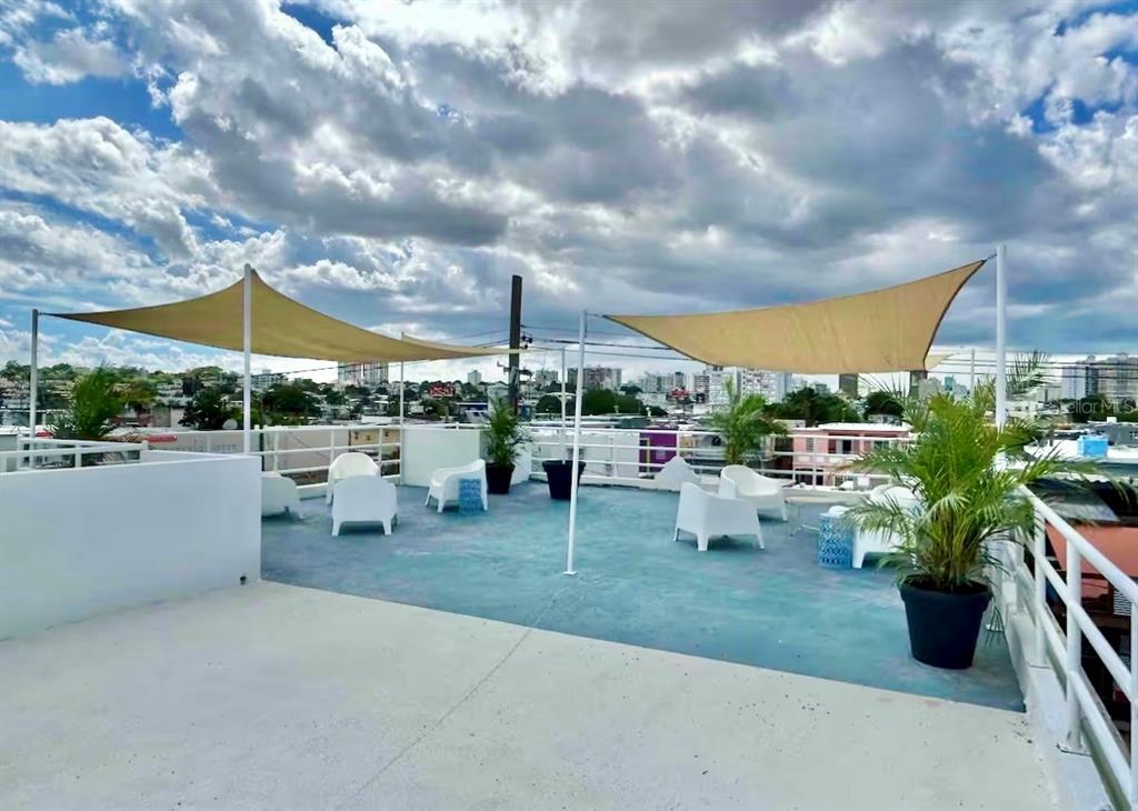 A rooftop terrace features white chairs, potted plants, and tan shade sails under a cloudy sky — 107 LOIZA, SAN JUAN, PR