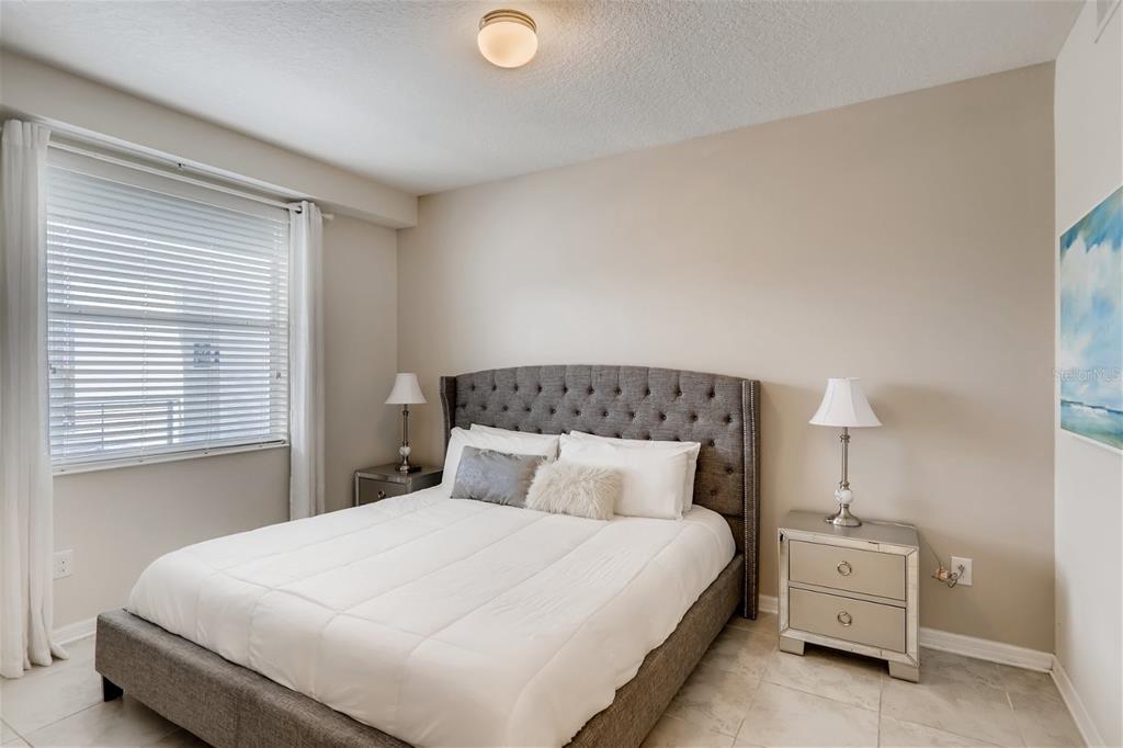 A bedroom features a tufted gray headboard, white bedding, and mirrored nightstands on tile flooring — 4731 CLOCK TOWER DRIVE UNIT 203, KISSIMMEE, FL