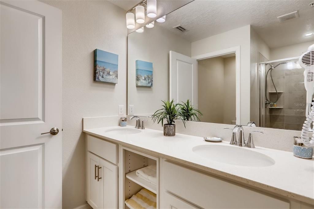 A bathroom features a double vanity with white cabinets, a large mirror, and a walk-in shower — 4731 CLOCK TOWER DRIVE UNIT 203, KISSIMMEE, FL