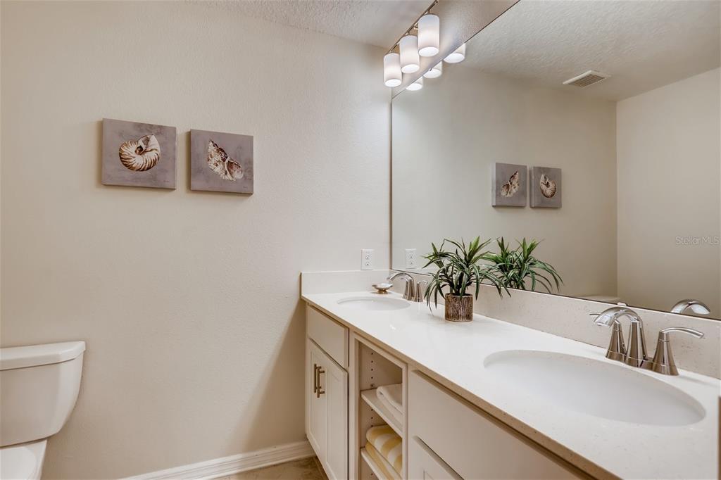 A bathroom features a double vanity with white cabinets, a large mirror, and seashell wall art — 4731 CLOCK TOWER DRIVE UNIT 203, KISSIMMEE, FL