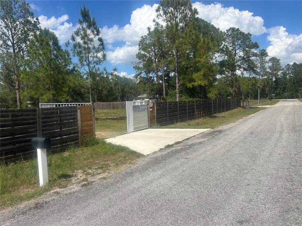 A fenced vacant lot with a concrete driveway and metal gate along a paved road — 4 EDEN CEMETERY ROAD, FROSTPROOF, FL