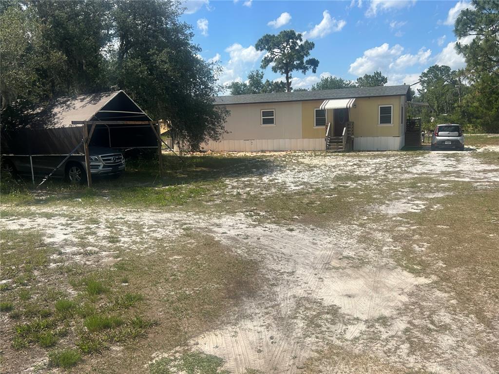 A single-story manufactured home with a carport and a sandy yard under a blue sky — 4 EDEN CEMETERY ROAD, FROSTPROOF, FL