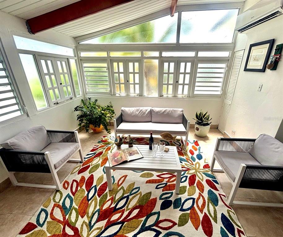 A sunroom features a colorful leaf-patterned rug, white patio furniture, and large windows — Punta Las Marias CAOBA 10 STREET UNIT 3, SAN JUAN, PR
