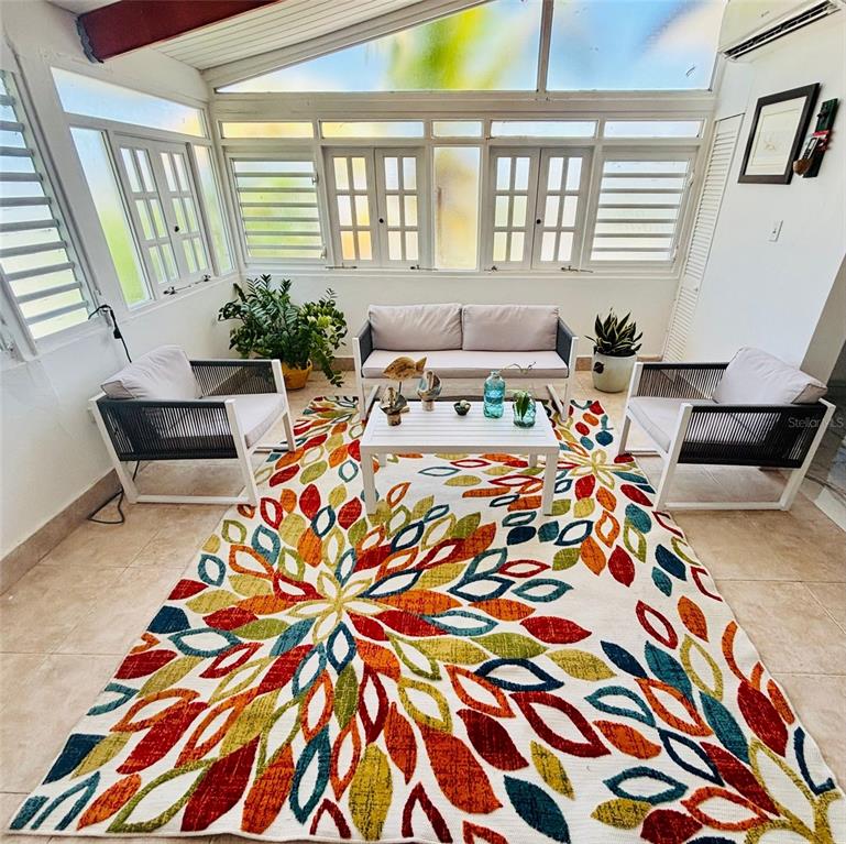 A sunroom features a colorful floral rug, a sofa, two armchairs, and large windows — Punta Las Marias CAOBA 10 STREET UNIT 3, SAN JUAN, PR