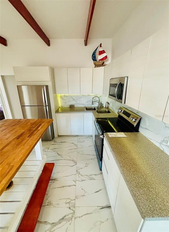 A kitchen features white cabinets, stainless steel appliances, marble-look tile flooring, and exposed ceiling beams — Punta Las Marias CAOBA 10 STREET UNIT 3, SAN JUAN, PR