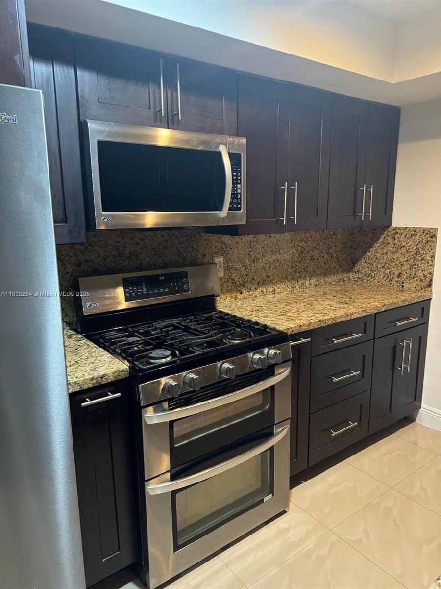 A kitchen features dark wood cabinets, granite countertops, and stainless steel appliances — 18101 NW 68th Ave # D207, Hialeah FL 33015, HIALEAH, FL