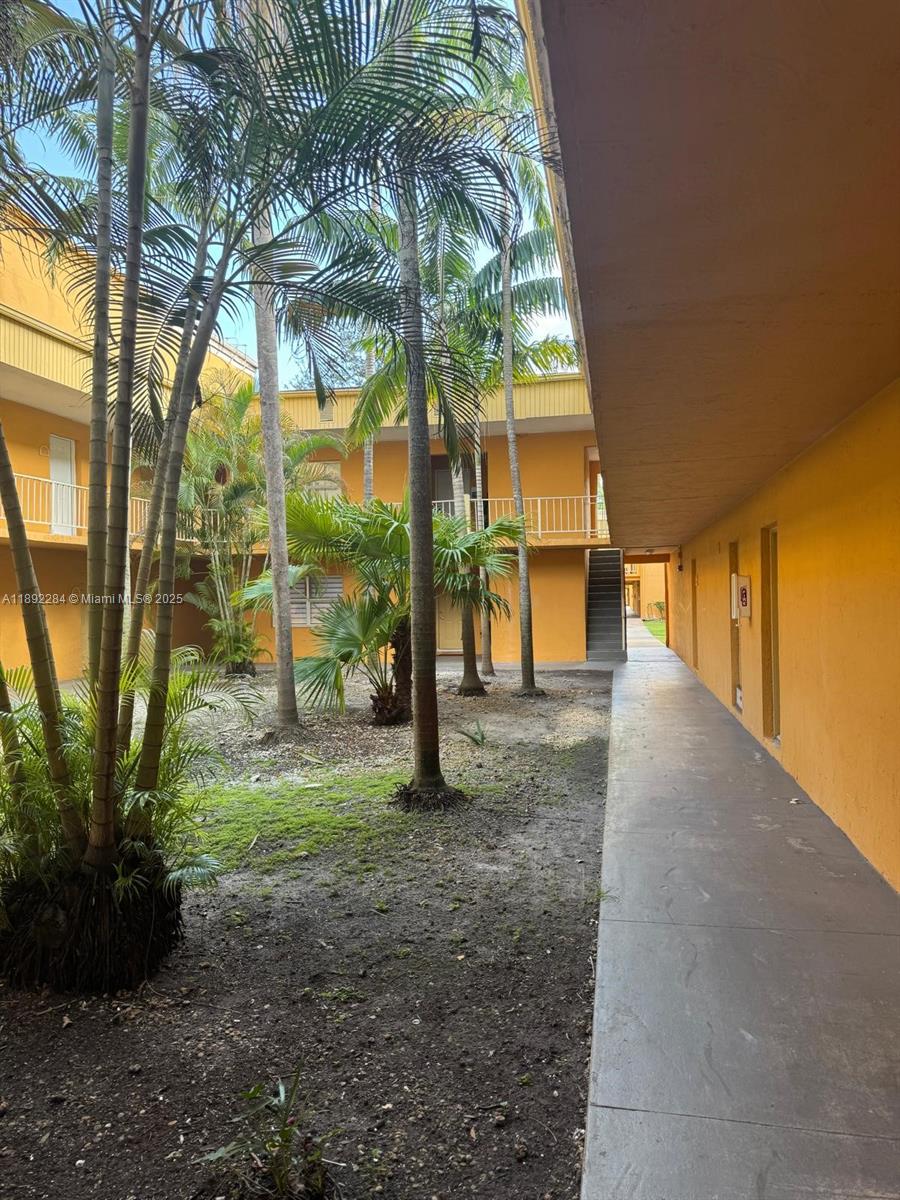 An outdoor walkway overlooks a courtyard with palm trees and yellow apartment building walls — 18101 NW 68th Ave # D207, Hialeah FL 33015, HIALEAH, FL