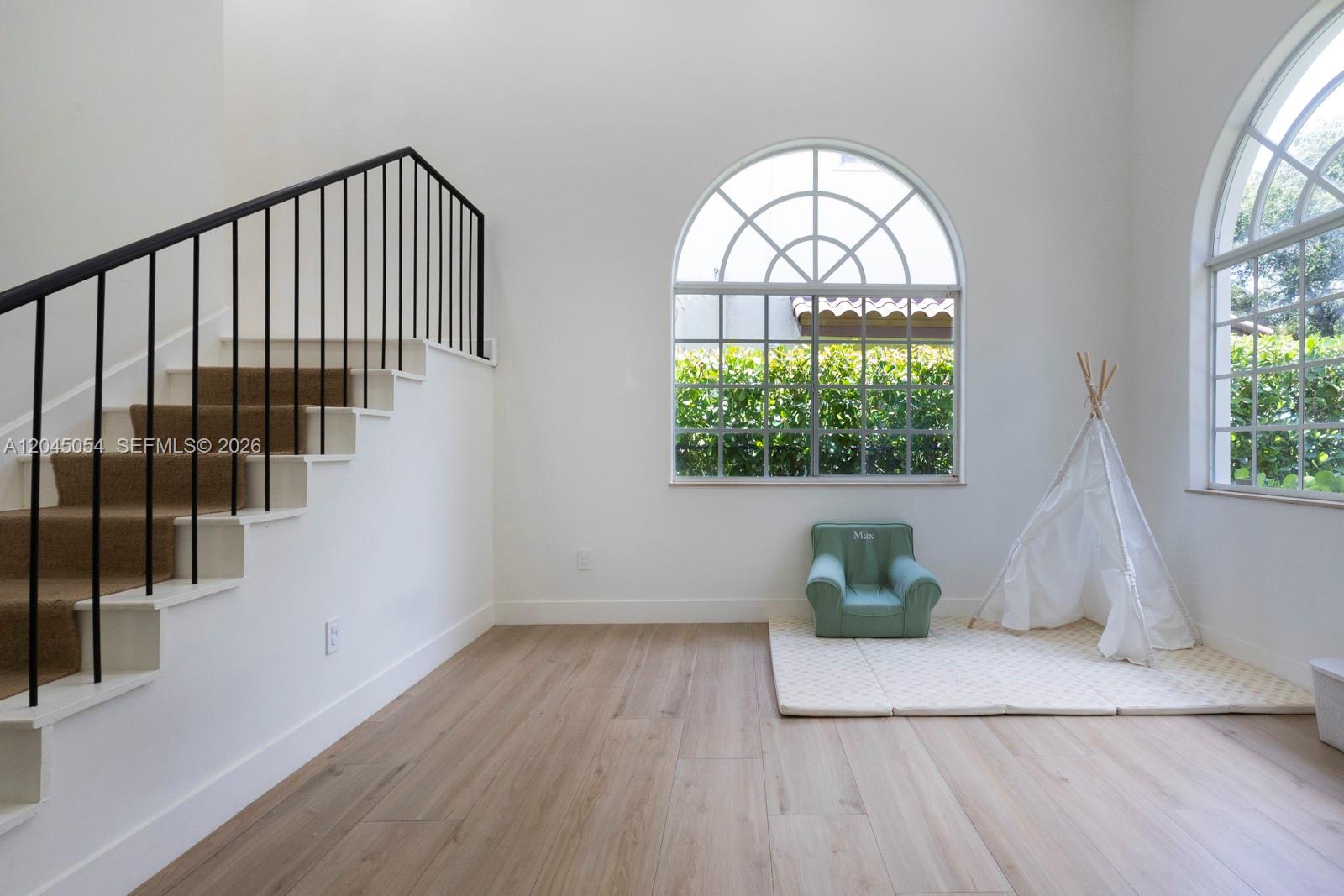 A bright room features light wood flooring, a staircase with black railings, and arched windows — 3908 Anderson Rd, Coral Gables FL 33134, CORAL GABLES, FL