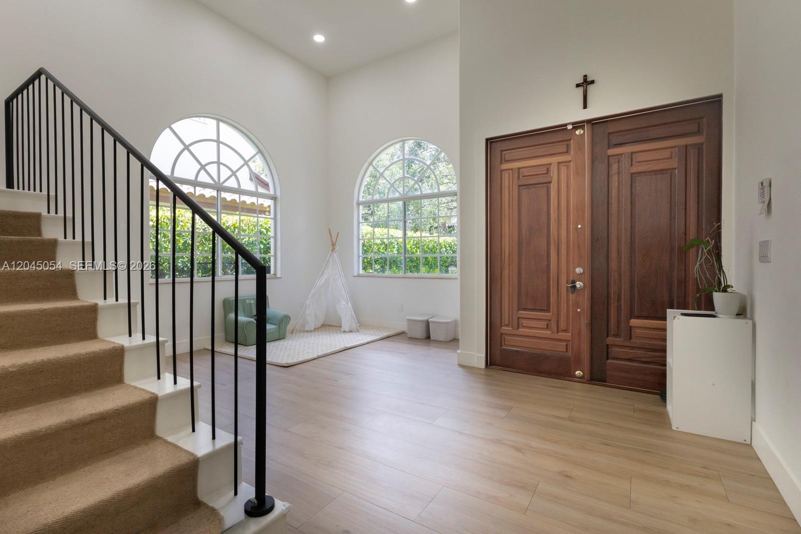 An entryway features a staircase, wood-look flooring, arched windows, and double wooden front doors — 3908 Anderson Rd, Coral Gables FL 33134, CORAL GABLES, FL