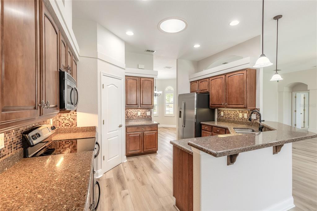 A kitchen features brown wood cabinets, granite countertops, stainless steel appliances, and light wood flooring — 3614 MARISOL COURT, NEW SMYRNA BEACH, FL