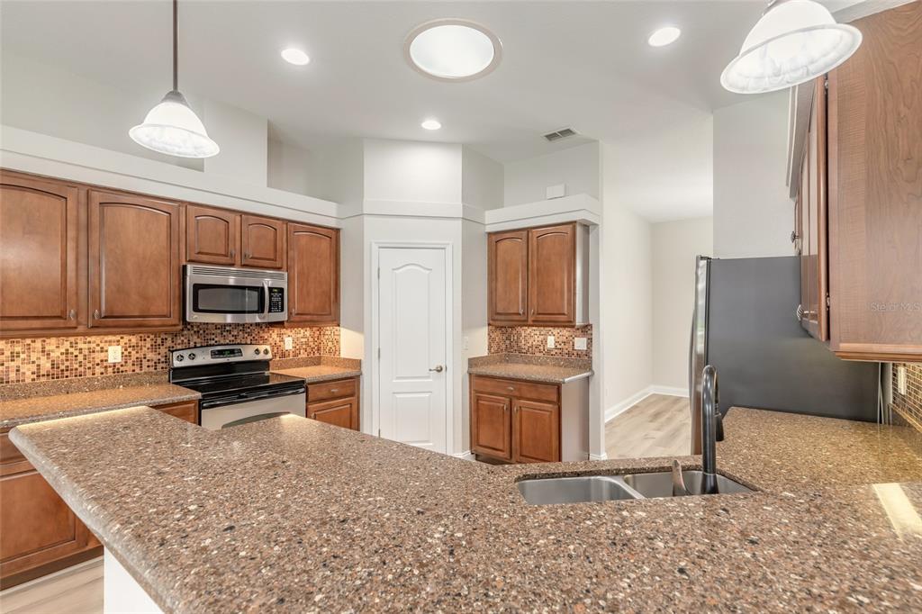 A kitchen features brown wood cabinets, speckled granite countertops, and stainless steel appliances — 3614 MARISOL COURT, NEW SMYRNA BEACH, FL