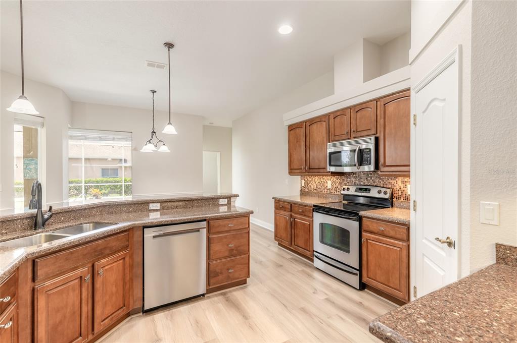 A kitchen features wood cabinets, granite countertops, stainless steel appliances, and light-colored wood flooring — 3614 MARISOL COURT, NEW SMYRNA BEACH, FL