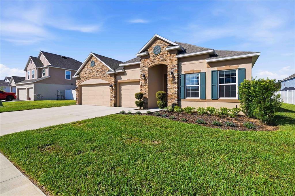 A single-story house with a stone facade, tan stucco, and a three-car garage — 925 FIELDSTONE WAY, HAINES CITY, FL