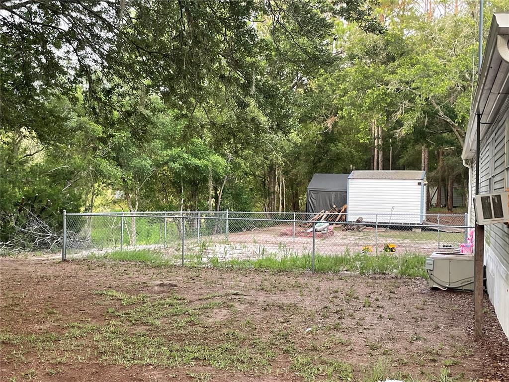 A fenced backyard features a small shed and a wooded area behind a mobile home — 8890 SE 66TH CIRCLE, TRENTON, FL