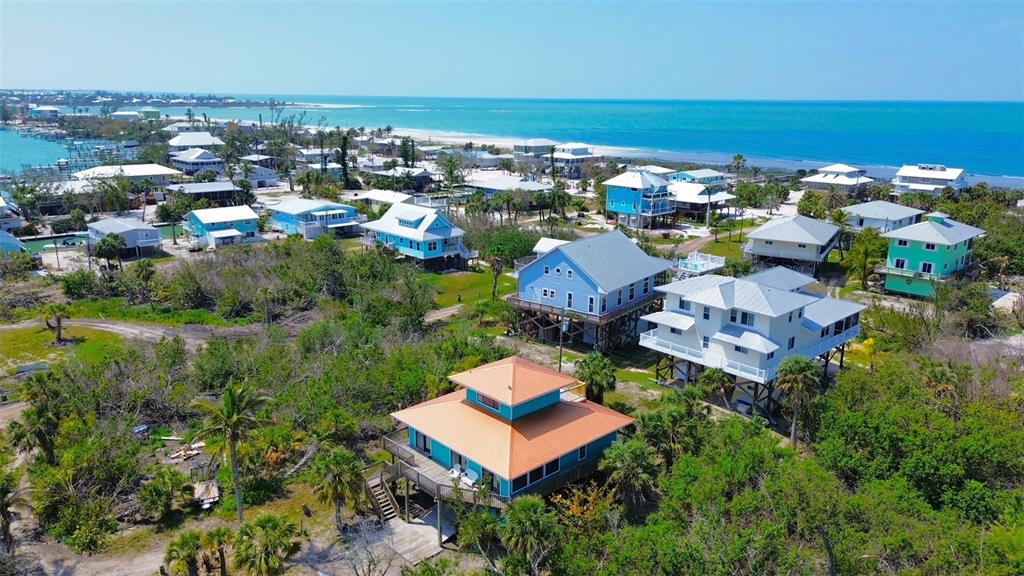 An aerial view shows several elevated coastal houses surrounded by lush vegetation near the ocean — 9580 ALMIRATE COURT, PLACIDA, FL