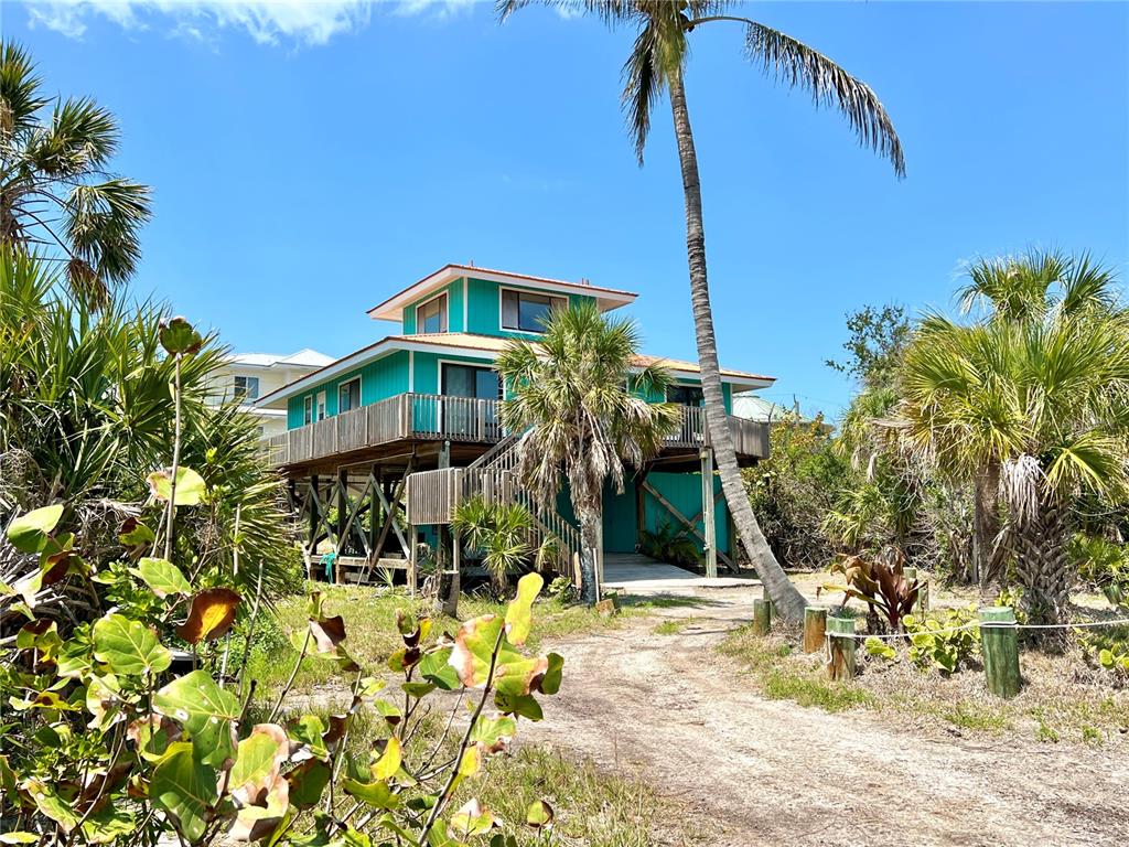 A teal, elevated house with a wrap-around deck stands among palm trees and sandy ground — 9580 ALMIRATE COURT, PLACIDA, FL