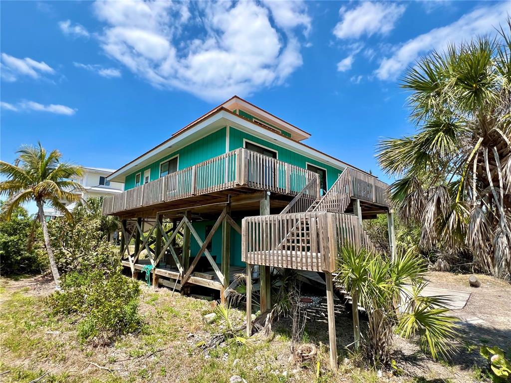 An elevated teal house with a wooden deck and staircase stands among palm trees — 9580 ALMIRATE COURT, PLACIDA, FL