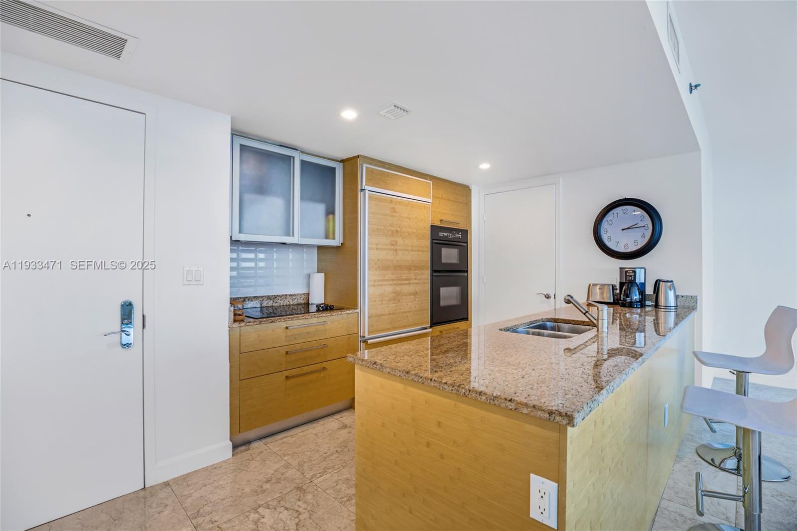 A modern kitchen features light wood cabinetry, granite countertops, and a breakfast bar with stools — 1830 S Ocean Dr # 4707, Hallandale Beach FL 33009, HALLANDALE BEACH, FL