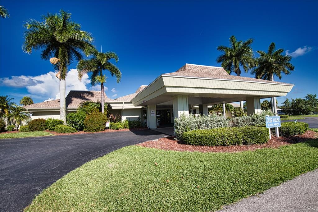 A low-slung clubhouse building features a large covered entryway, palm trees, and manicured landscaping — 207 LA ROSAS, NORTH PORT, FL