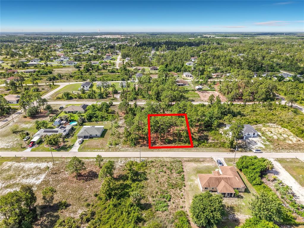 An aerial view shows a rectangular vacant lot outlined in red within a wooded neighborhood — 722 MANUEL STREET E, LEHIGH ACRES, FL