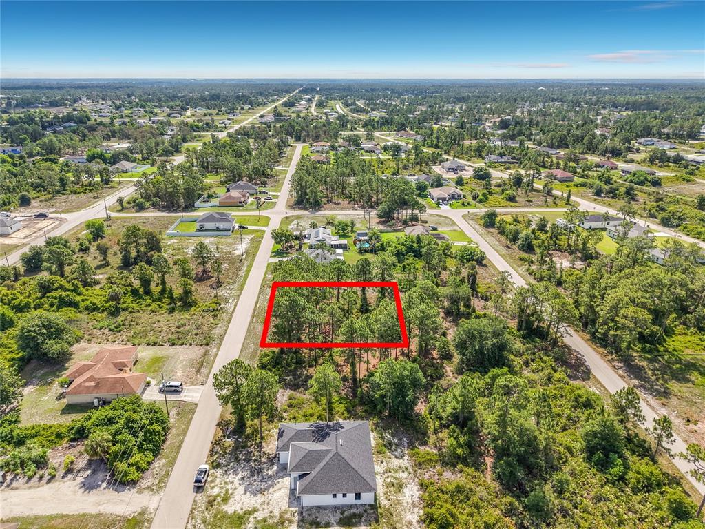 An aerial view shows a rectangular, wooded vacant lot outlined in red within a neighborhood — 722 MANUEL STREET E, LEHIGH ACRES, FL