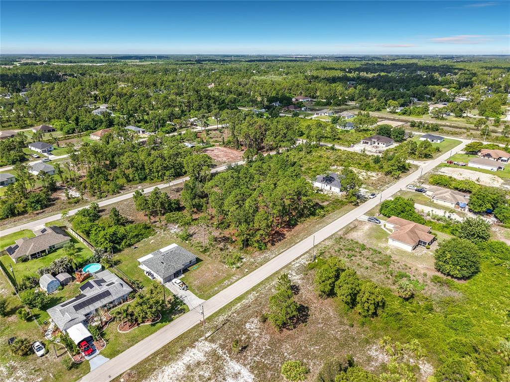 An aerial view shows a residential neighborhood with scattered houses, wooded lots, and paved roads — 722 MANUEL STREET E, LEHIGH ACRES, FL