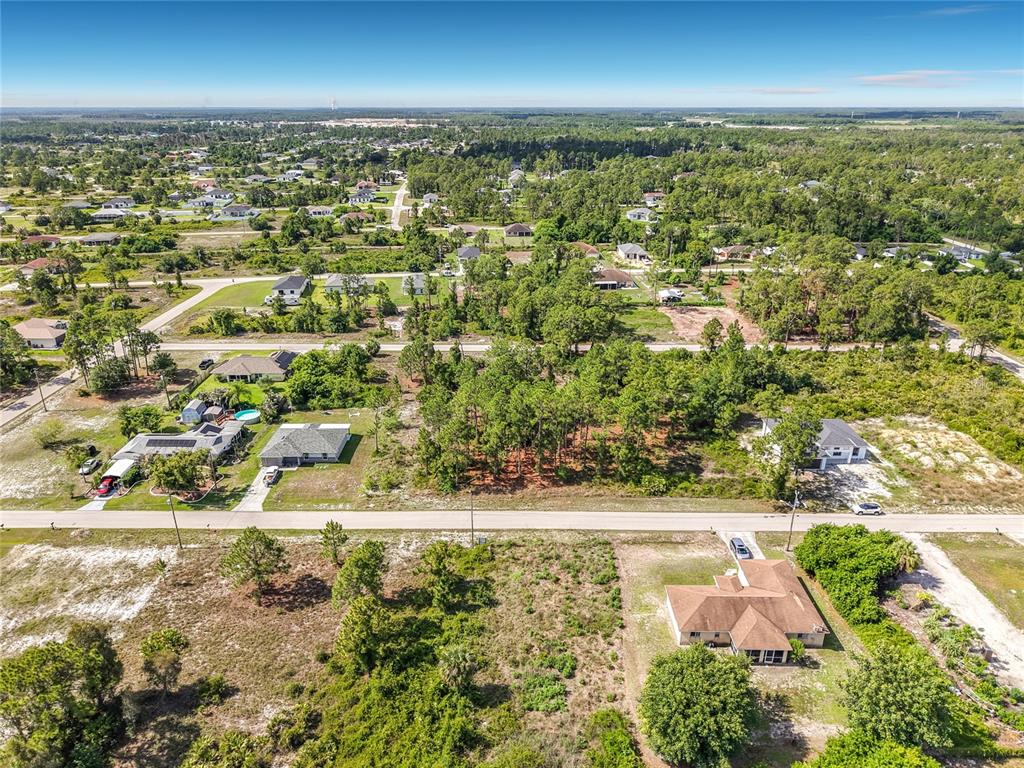 An aerial view shows a residential neighborhood with scattered houses, wooded lots, and paved roads — 722 MANUEL STREET E, LEHIGH ACRES, FL