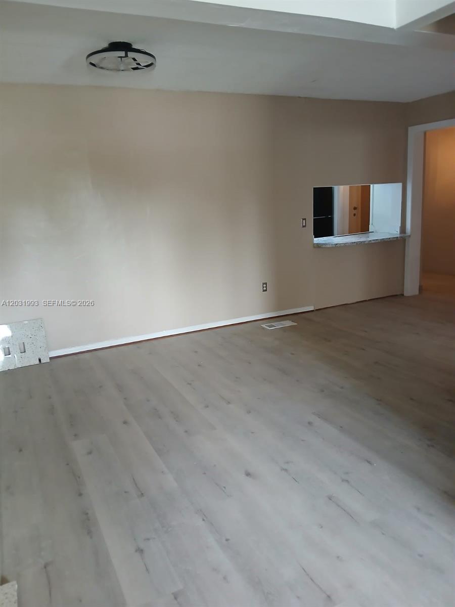 An empty room features light-colored wood-look flooring, beige walls, and a kitchen pass-through window — 1400 NE 148th St # 2, Miami FL 33161, MIAMI, FL