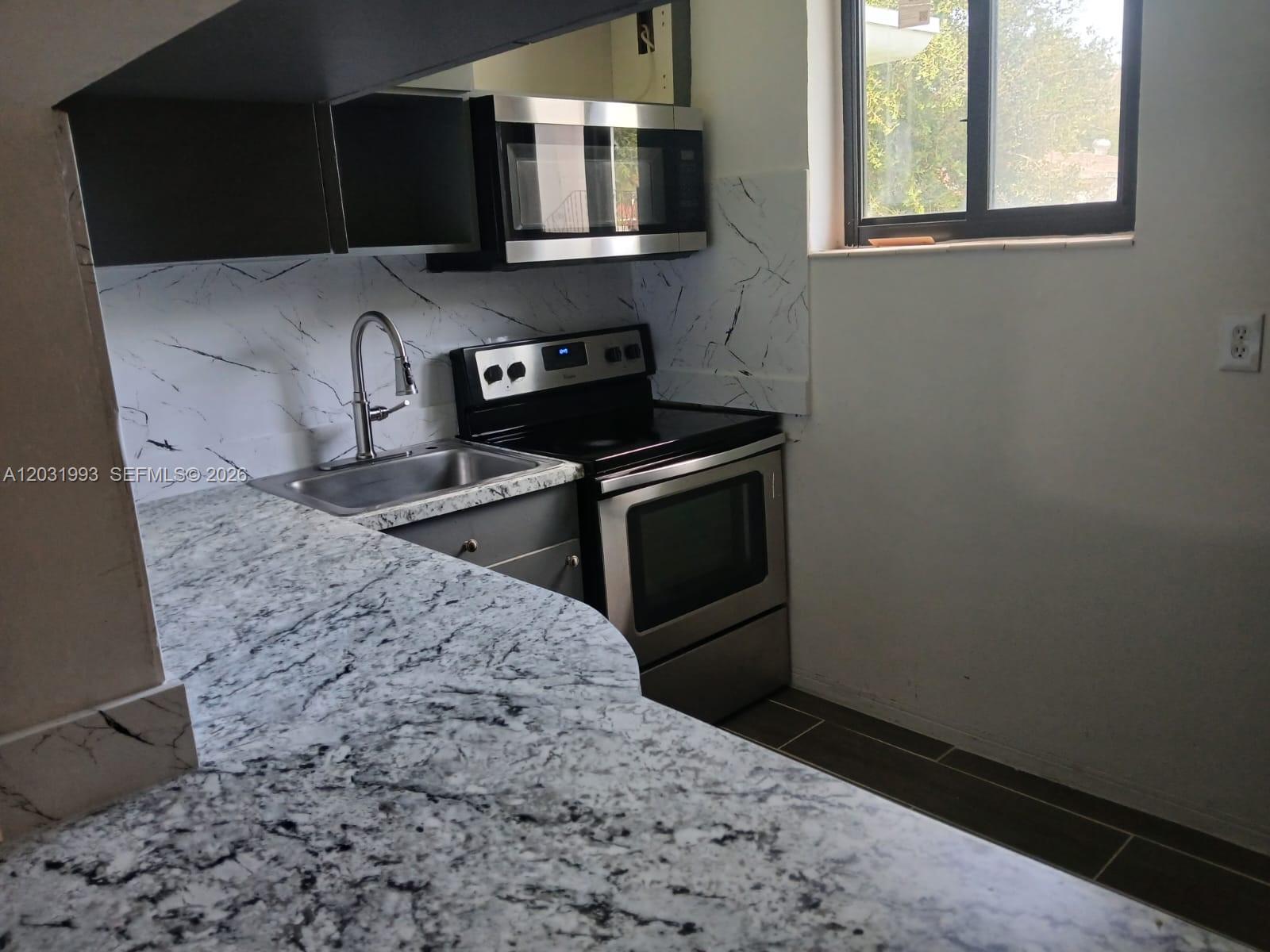 A kitchen features granite countertops, a stainless steel stove, a microwave, and marble-patterned backsplashes — 1400 NE 148th St # 2, Miami FL 33161, MIAMI, FL