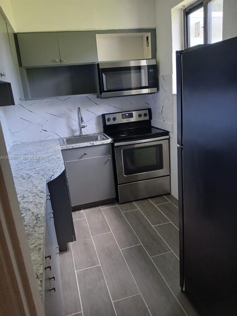 A small kitchen features gray cabinets, stainless steel appliances, and a marble-patterned backsplash — 1400 NE 148th St # 2, Miami FL 33161, MIAMI, FL
