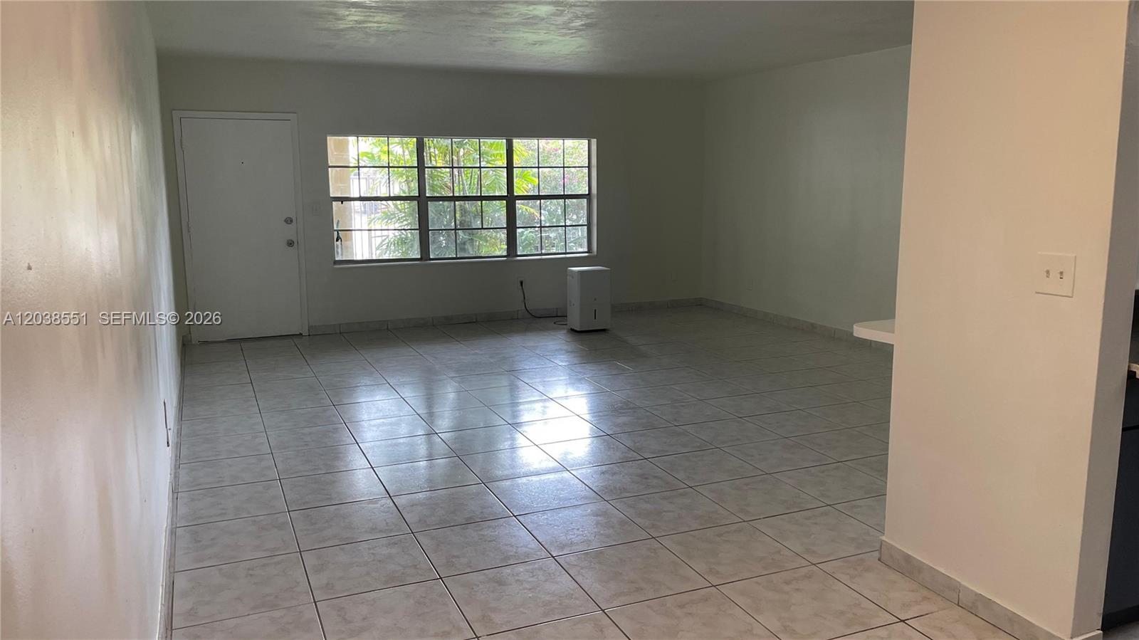 An empty room features light-colored tile flooring, white walls, and a large window — 1855 NE 121st St # 2, North Miami FL 33181, NORTH MIAMI, FL