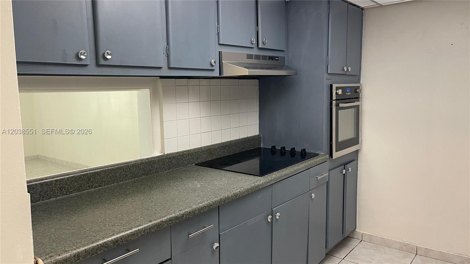 A kitchen features blue cabinets, a black cooktop, a wall oven, and a pass-through window — 1855 NE 121st St # 2, North Miami FL 33181, NORTH MIAMI, FL