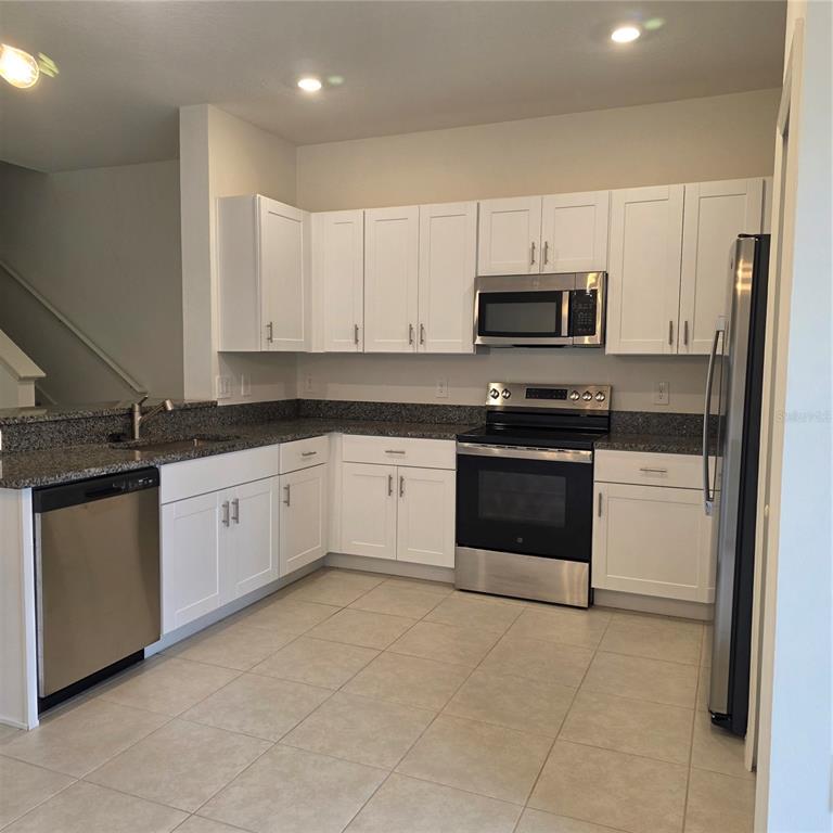 A kitchen features white cabinets, granite countertops, stainless steel appliances, and light tile flooring — 6076 SHINER STREET, LAND O LAKES, FL