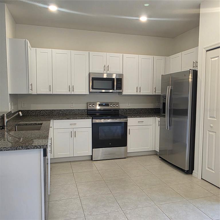 A kitchen features white cabinets, granite countertops, stainless steel appliances, and light tile flooring — 6076 SHINER STREET, LAND O LAKES, FL